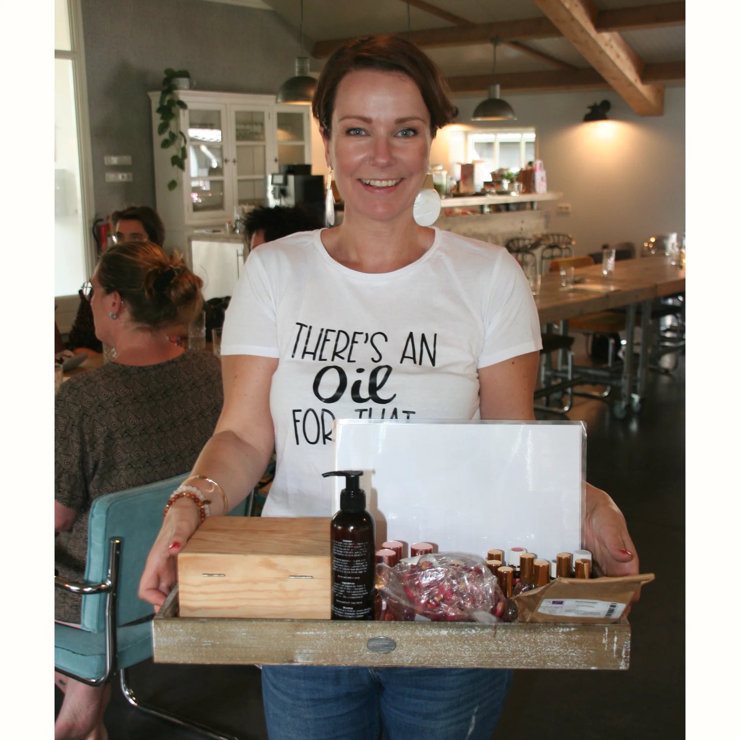 Suzanne glimlachend met een dienblad vol Young Living producten en cadeautjes voor de goodiebags, gekleed in een T-shirt met de tekst ‘There’s an oil for that’. Enthousiasme voor natuurlijke gezondheid en welzijn!