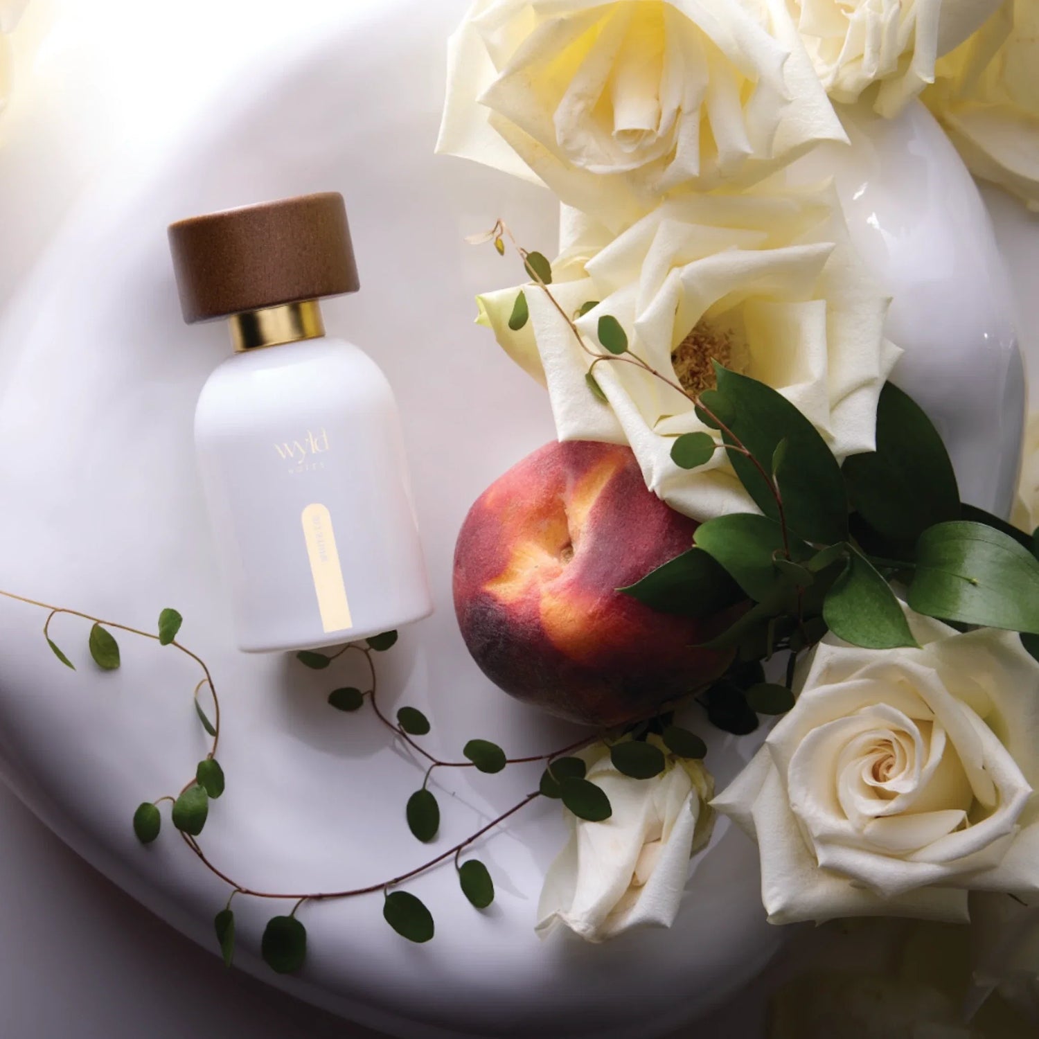 Wyld Notes White Lie eau de parfum in witte flacon met perziken, roomwitte rozen en groen blad.