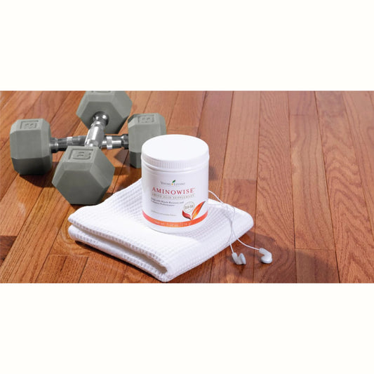 Young Living AminoWise supplement op een witte handdoek naast gewichten – ideaal bij herstel na burn-out, spanningshoofdpijn en overspanning.