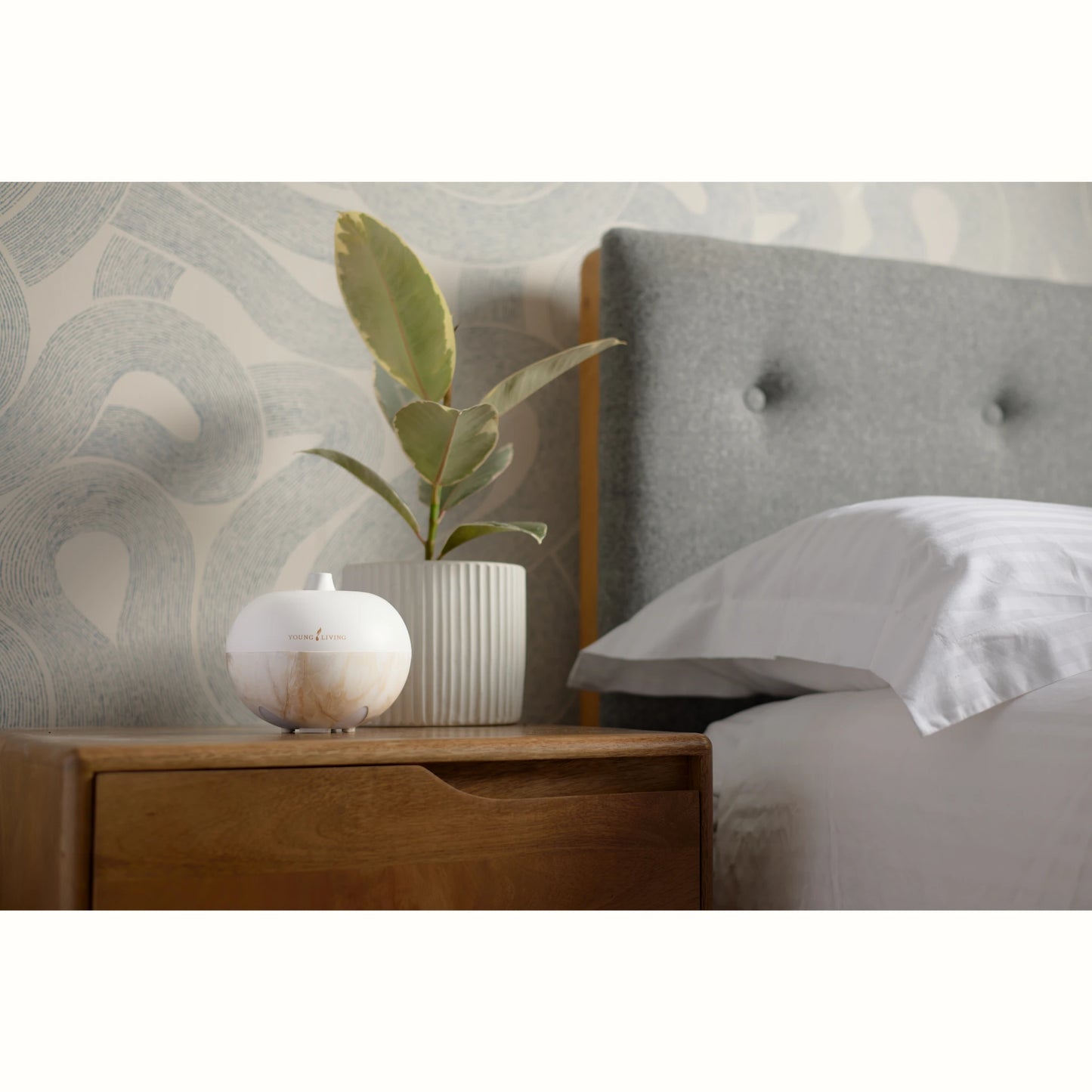 De AromaGlobe diffuser van Young Living staat op een nachtkastje in een stijlvol interieur en verspreidt etherische oliën die de lucht zuiveren – ideaal tegen schimmels, geurtjes en voor een frisse slaapkameromgeving.