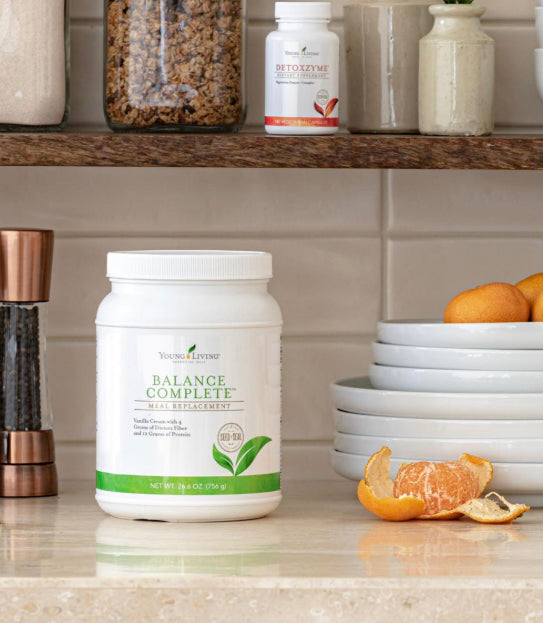Young Living Balance Complete maaltijdvervanger op een keukenblad met fruit en servies – voedzame shake met proteïne en vezels voor een gebalanceerde levensstijl.