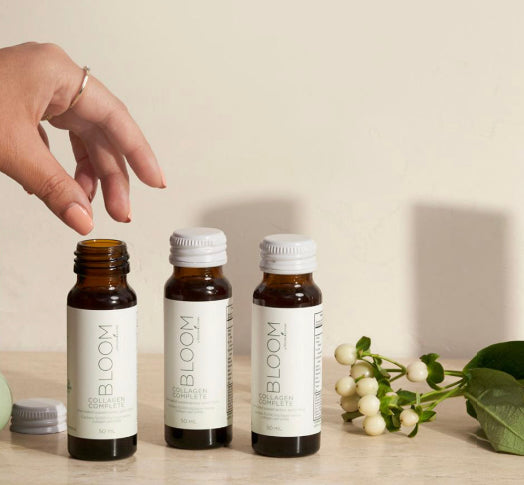 Drie flesjes Bloom Collagen Complete van Young Living op een marmeren blad – vloeibare collageenboost voor huid, haar en nagels, met frisse botanische styling.