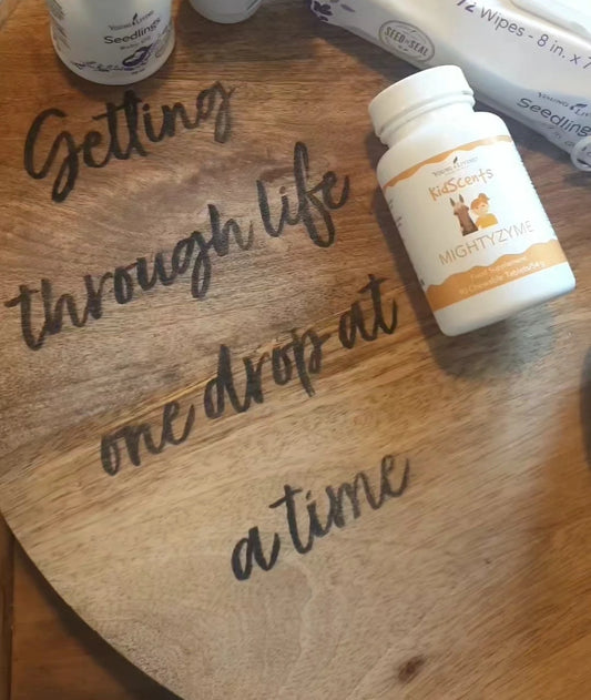 Young Living KidScents MightyZyme supplement tussen natuurlijke verzorging, op een houten blad met de tekst: “Getting through life one drop at a time.”