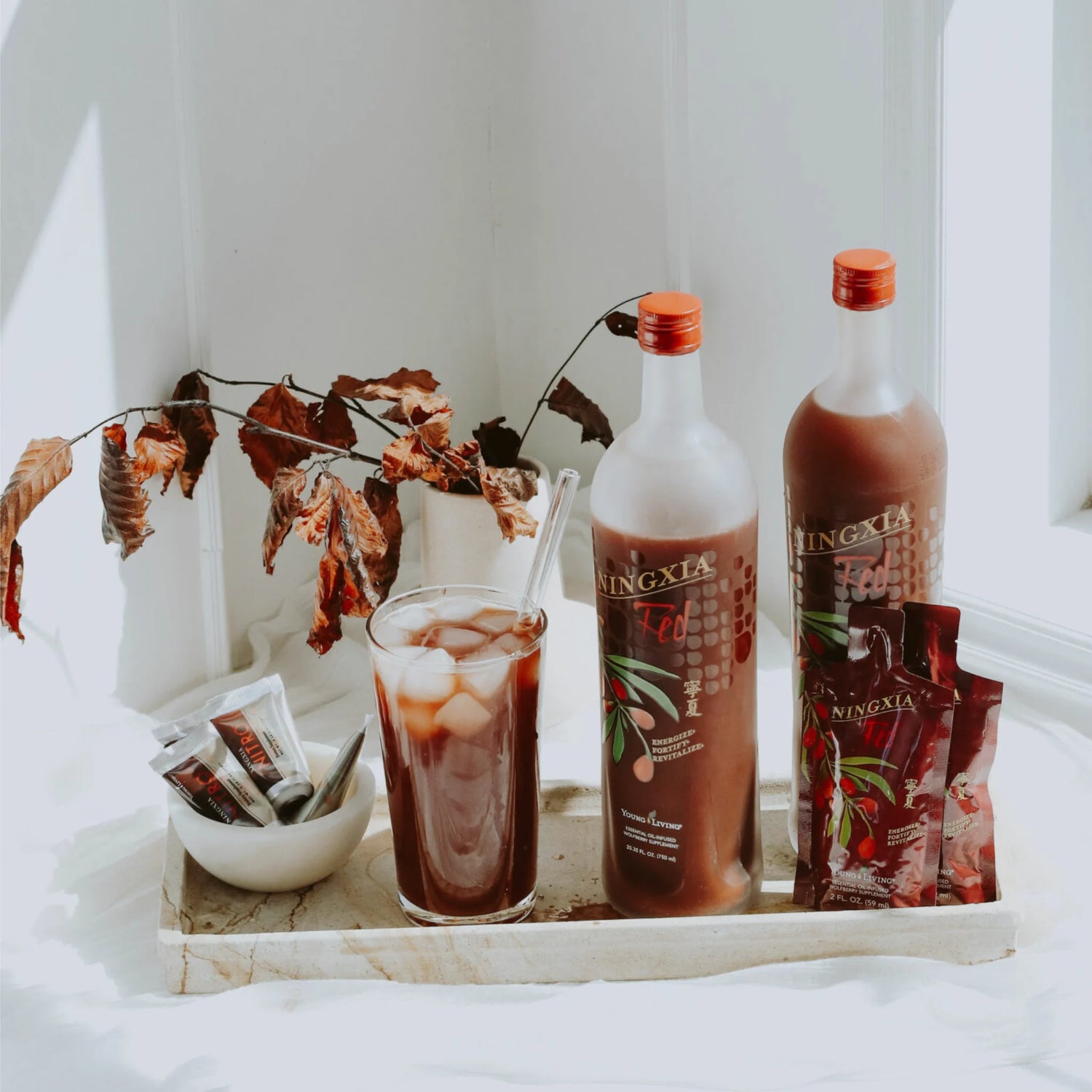 Verschillende NingXia-producten van Young Living, waaronder drinkpakjes en flessen, naast een glas NingXia met ijsblokjes op een dienblad. Verfrissende antioxidanten boost voor energie en welzijn.