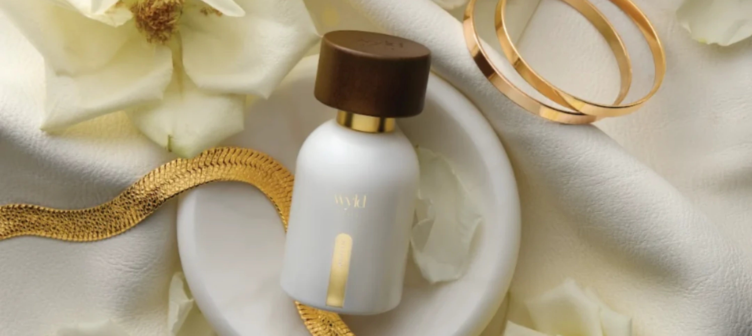 White Lie flacon op een lichte kaptafel met zachte rozen, geranium, zijde, gouden sieraden, warm daglicht en quiet luxury uitstraling. Volwassen vrouwelijk, zacht romantisch en niet bridal.