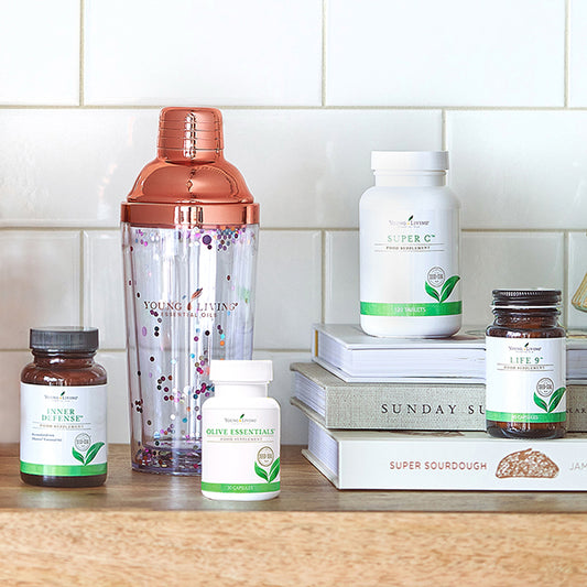 Variatie aan voedingssupplementen op een houten plank, met boeken en een transparante shaker, als symbool voor consistente maandelijkse zelfzorg en investeren in je gezondheid.