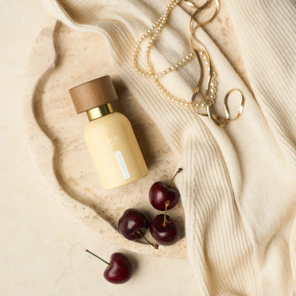Wyld Notes Cashmere Crème parfum tussen zachte crèmekleurige stof, kersen en sieraden in een elegante lifestyle-setting.