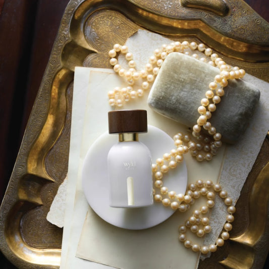 Wyld Notes White Lie parfumflacon op een antieke goudkleurige schaal met parels, een crèmekleurig fluwelen etui en papier.